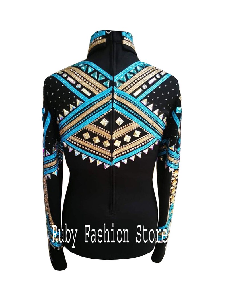 Op de afbeelding: Een zwart shirt met lange mouwen, een hoge kraag en ingewikkelde geometrische patronen in turquoise, goudkleurige en heldere kristallen. Het ontwerp bevat rijen strass-steentjes en studs op de schouders en rug. Tekst: Ruby Fashion Store.