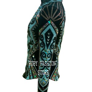 May include: A black long-sleeved shirt featuring intricate light blue patterns, embellished with numerous iridescent crystals and beads. The garment displays the text RUBY FASHION STORE in white lettering on the side, showcasing a high-neck design.