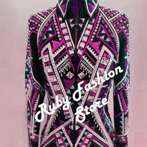 May include: A black jacket with fuchsia and white geometric patterns, featuring a front zipper, a high collar, and extensive embellishments of silver studs and clear crystals. The text "Fuchsia on Black Base" and "Ruby Fashion Store" is visible.