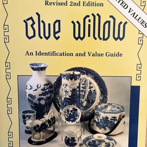 May include: A book titled "Blue Willow: An Identification and Value Guide" with a yellow cover and a white sticker that says "Updated Values". The book is a revised 2nd edition and features a collection of blue and white willowware china.