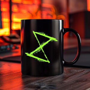 May include: Black coffee mug with a neon green geometric design. The design is a stylized hourglass shape with a textured, speckled appearance. The mug has a rounded body and a large, curved handle.