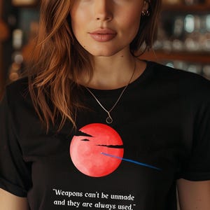 May include: Black t-shirt featuring a red planet design with a blue laser beam and the quote: "Weapons can't be unmade and they are always used." The shirt is made of a soft material.
