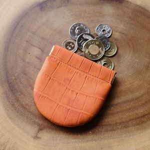 May include: A small orange leather coin purse with a crocodile pattern, open and spilling out a pile of coins.