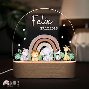 Könnte beinhalten: Nachtlicht mit Holzsockel und klarer Acrylfront. Auf dem Acryl stehen der Name "Felix" und das Datum "27.12.2016". Darunter ein Regenbogen und Zeichentricktiere: ein Nilpferd, ein Löwe, ein Elefant, ein Zebra und eine Giraffe. Der Sockel hat das Logo "LARIFEE".