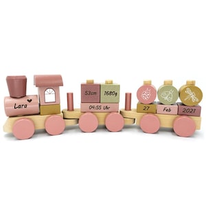 Peut inclure: Un train en bois rose jouet avec un nom personnalisé "Lara" sur la locomotive. Les wagons du train présentent des détails comme un cœur, une fenêtre et une coccinelle. Le train comprend également des blocs avec la date et l'heure de naissance, les mesures et le mot "fév".