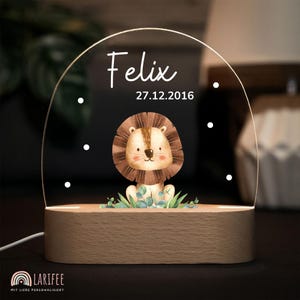 Könnte beinhalten: Ein Nachtlicht mit Holzsockel und einem klaren Acrylbogen. Das Acryl zeigt den Namen "Felix" und das Datum "27.12.2016" in Weiß. Eine Cartoon-Löwen-Illustration ist auf dem Acryl zentriert. Der Sockel hat ein warmes Leuchten.