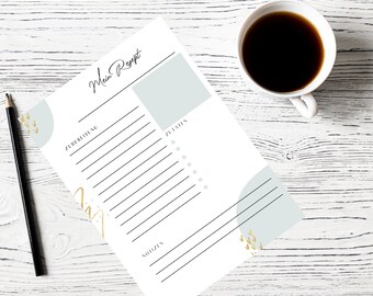 May include: A recipe sheet with the words "Mein Rezept" in script. The sheet has sections for preparation, ingredients, and notes, with a light blue and gold design. A cup of coffee and a pencil are next to the sheet.