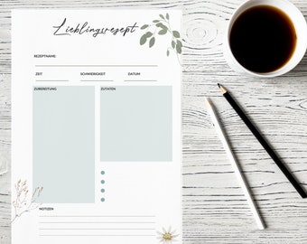May include: A white recipe sheet with the word "Lieblingsrezept" in script. The sheet has sections for recipe name, time, difficulty, date, preparation, ingredients, and notes. A cup of coffee and two pencils are on the right.