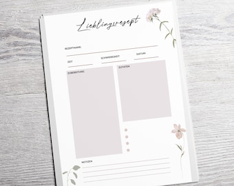 May include: A white recipe notepad with the word "Lieblingsrezept" in cursive script. The notepad features sections for recipe name, time, difficulty, ingredients, and notes. Floral illustrations in soft pink and green adorn the corners.