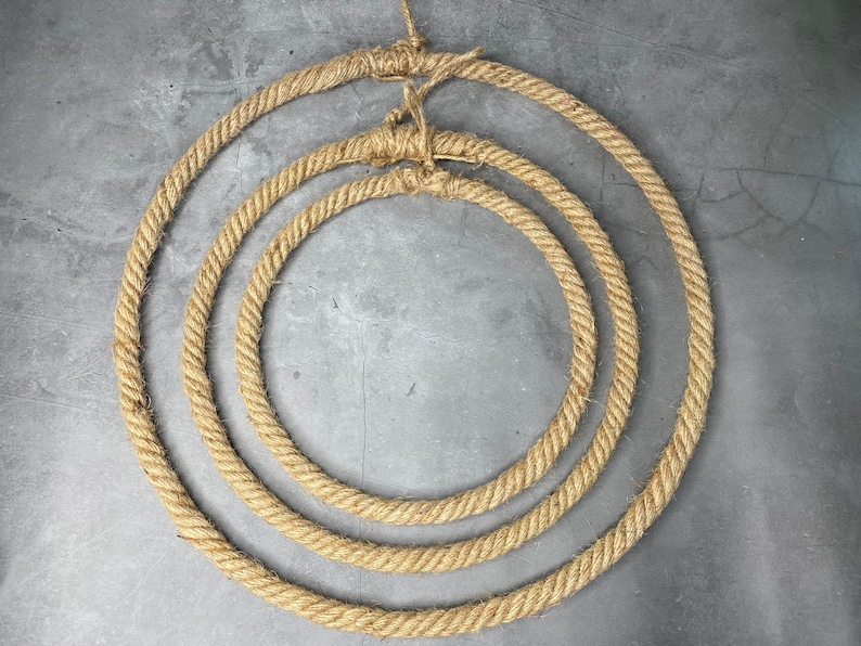 May include: Three concentric circles made of natural brown rope, creating a decorative wreath or wall hanging.