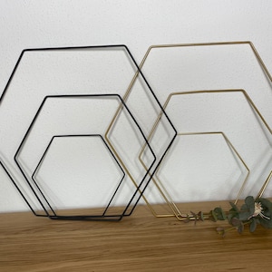Puede incluir: Conjunto de cuatro aros geométricos de metal en negro y dorado. Los aros están dispuestos en un patrón anidado, con el aro más grande en la parte inferior y el más pequeño en la parte superior. Los aros están hechos de metal delgado y tienen un diseño simple y moderno.