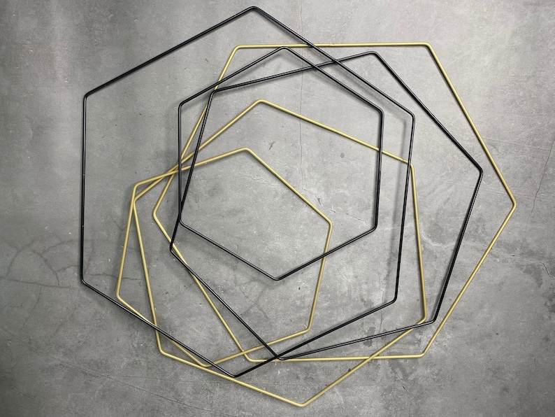 May include: A set of five geometric shapes, four black and one gold, are arranged in a concentric pattern. The shapes are all octagons, with the gold octagon in the center.
