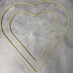 May include: Two gold metal heart-shaped hoops, one inside the other, against a gray background.