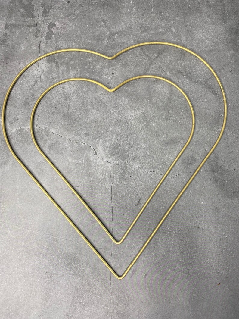 May include: Two gold metal heart-shaped hoops, one inside the other, against a gray background.