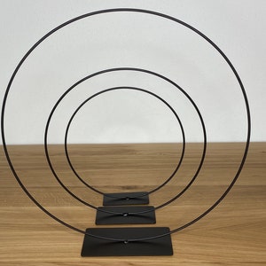 May include: Three black metal hoops of different sizes, stacked on top of each other, with a black base.