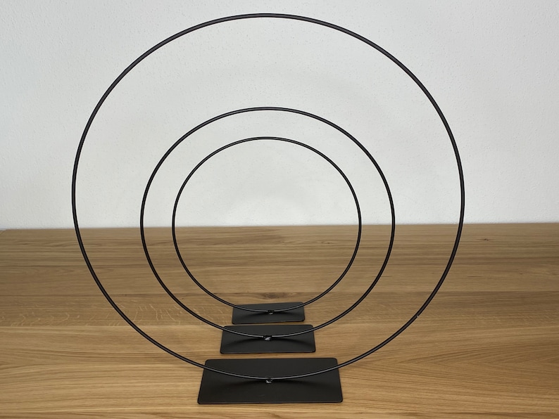 May include: Three black metal hoops of different sizes, stacked on top of each other, with a black base.