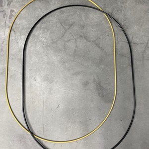 May include: Two metal hoops, one gold and one black, are overlapping on a gray background. The hoops are circular and have a smooth, polished finish.