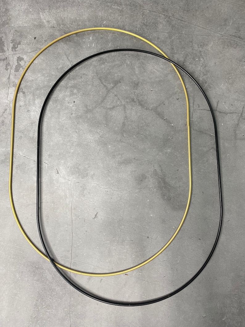 May include: Two metal hoops, one gold and one black, are overlapping on a gray background. The hoops are circular and have a smooth, polished finish.