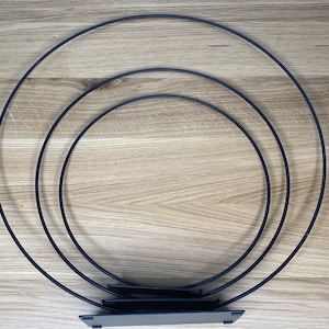 May include: Three black metal hoops of different sizes stacked on top of each other. The hoops are connected by a flat black metal base.