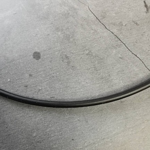 May include: A close-up of a black electrical cord on a gray textured surface.