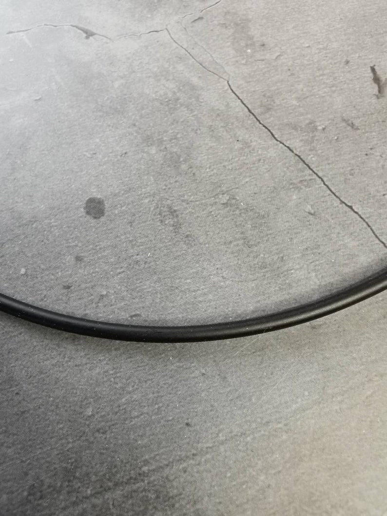 May include: A close-up of a black electrical cord on a gray textured surface.