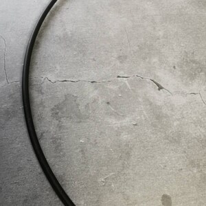 May include: A black metal hoop, possibly for a craft project or a decorative element, is lying on a gray concrete surface.