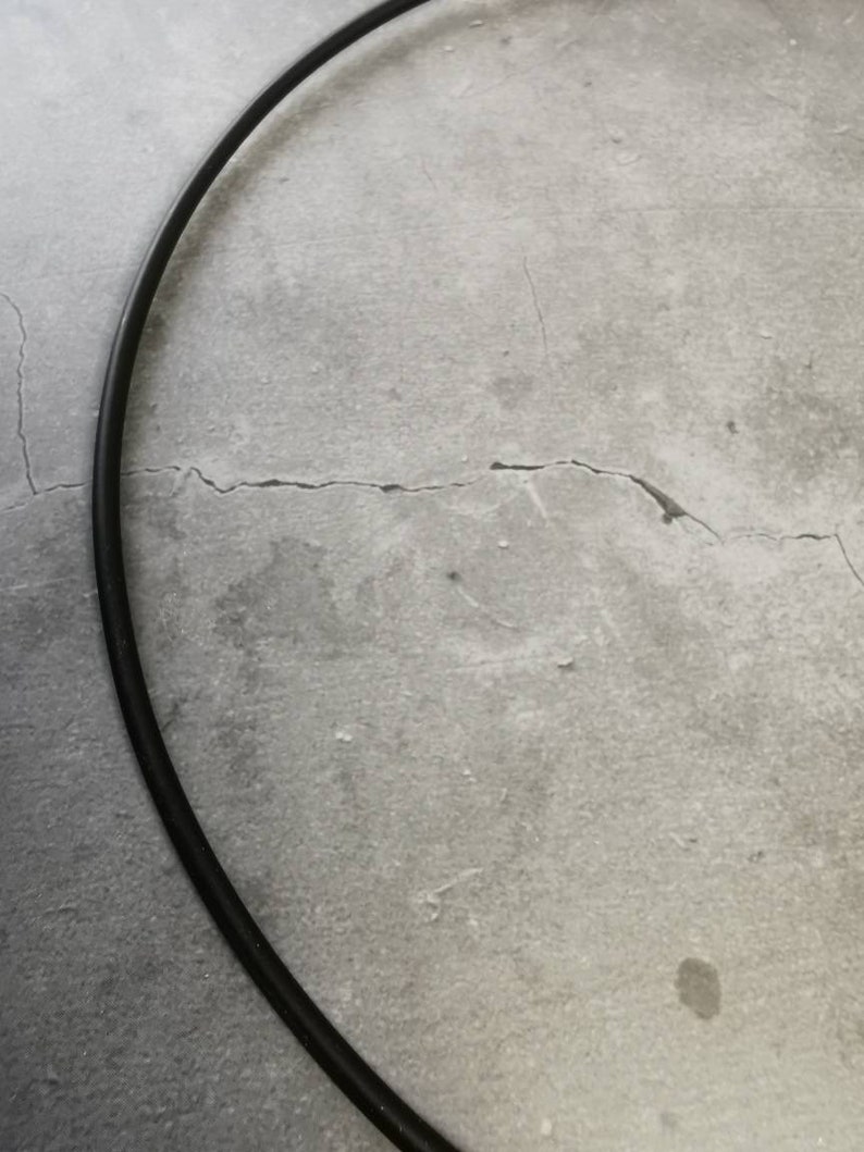 May include: A black metal hoop, possibly for a craft project or a decorative element, is lying on a gray concrete surface.