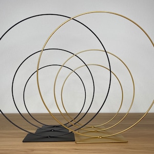 May include: A set of five metal hoops, three gold and two black, arranged in a concentric circle pattern. The hoops are connected to a base, creating a decorative display.
