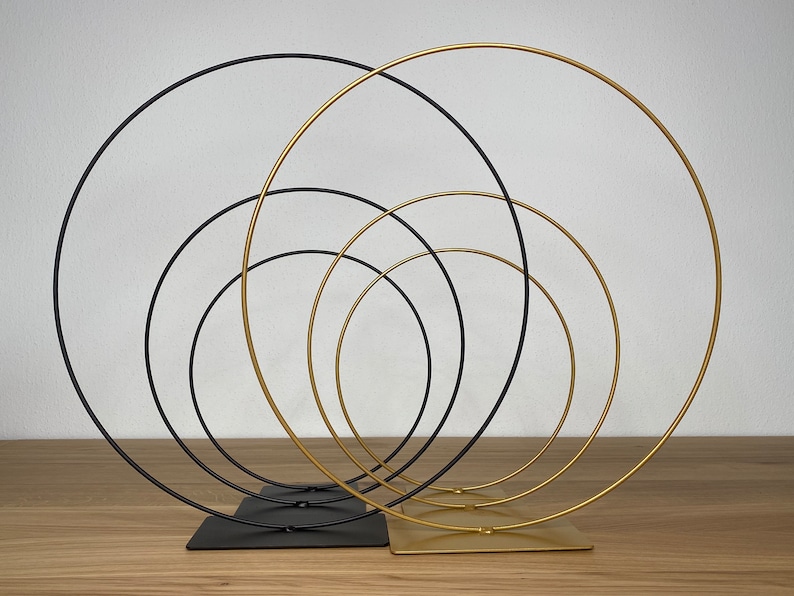 May include: A set of five metal hoops, three gold and two black, arranged in a concentric circle pattern. The hoops are connected to a base, creating a decorative display.