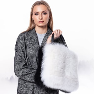 Può includere: Una borsa tote in pelliccia bianca e nera con manico in pelle nera. La borsa è tenuta da una persona che indossa un cappotto a quadri grigi.
