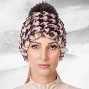 May include: A brown and white patterned fur hat with a brown fur pom pom on top.