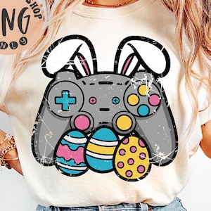 May include: A white t-shirt with a gray video game controller with bunny ears and colorful Easter eggs. The controller has a plus sign and other buttons.