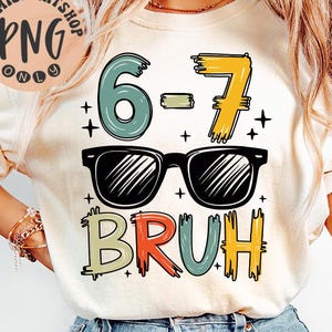 Może przedstawiać: Kremowa koszulka z nadrukiem graficznym przedstawiającym liczby "6-7", okulary przeciwsłoneczne i słowo "BRUH" w kolorowych literach. Koszulka jest połączona z niebieskimi dżinsami.