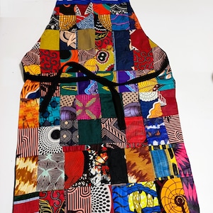 Peut inclure: Un tablier coloré en patchwork avec une ceinture noire et une bordure bleue. Le tablier est fait de différents tissus avec des motifs et des couleurs variés.