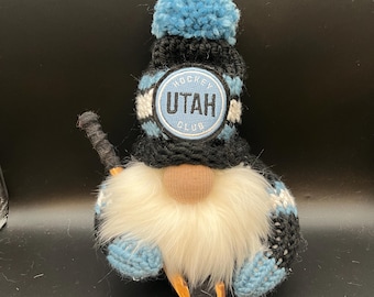 May include: A blue and black gnome wearing a hat with the words "Hockey Utah Club" on it. The gnome is holding a hockey stick.