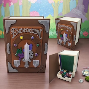 May include: A brown wooden book-shaped box with a metal latch and the word "Enchiridion" on the front. The box is open to reveal a green felt-lined compartment with dice inside.