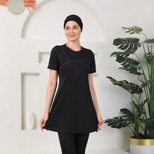 Puede incluir: Un traje de baño negro con ribete morado. El traje de baño tiene una parte superior de manga larga y pantalones largos. La modelo lleva un pañuelo negro en la cabeza.