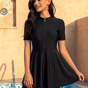 Peut inclure: Un haut de maillot de bain noir uni avec un col montant, des manches courtes et une fermeture éclair frontale. Le vêtement présente un corsage ajusté qui se termine par un ourlet évasé style basque, offrant une silhouette structurée pour la baignade.