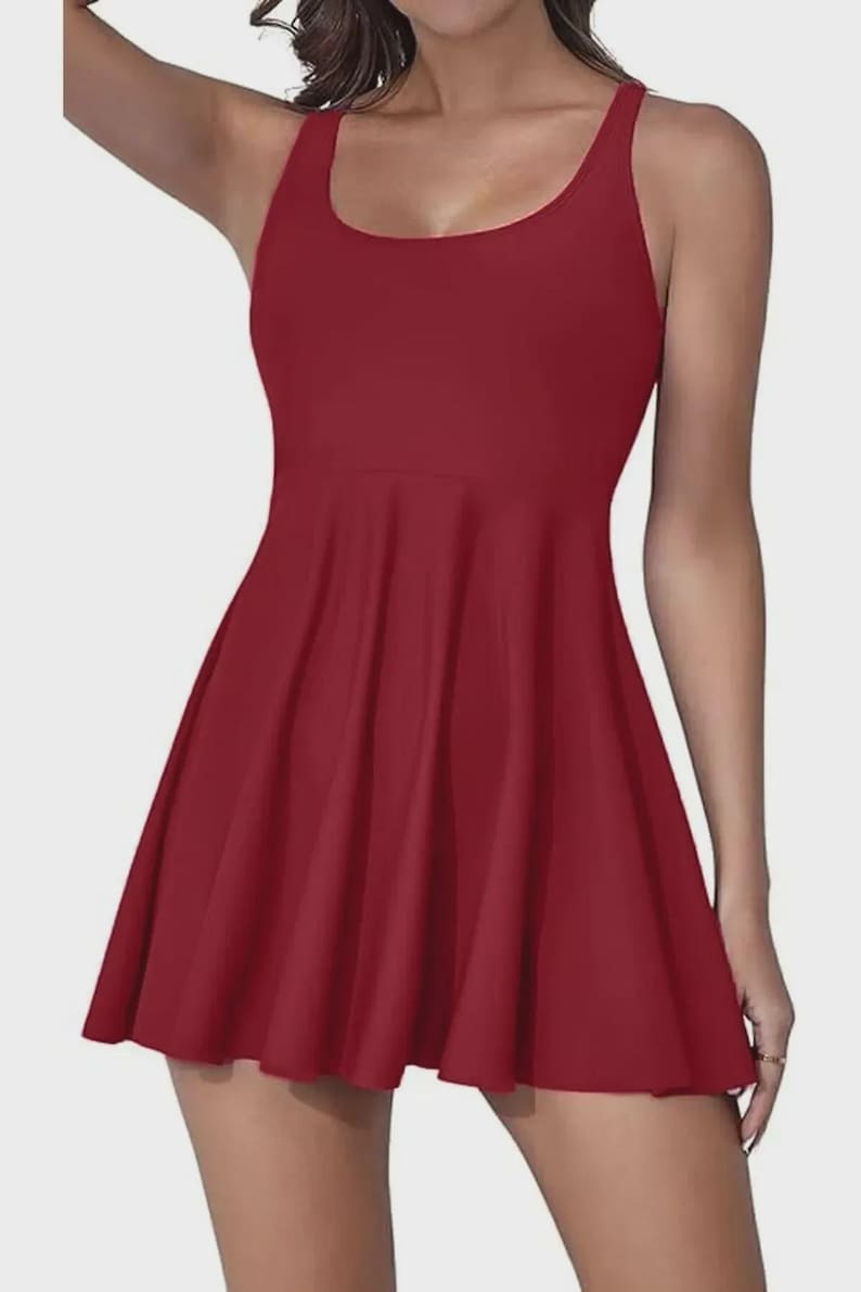 May include: A solid burgundy skater dress with a scoop neckline and thin straps. The dress features a fitted bodice and a flared skirt, creating a flattering silhouette. The fabric appears smooth and has a slight sheen.