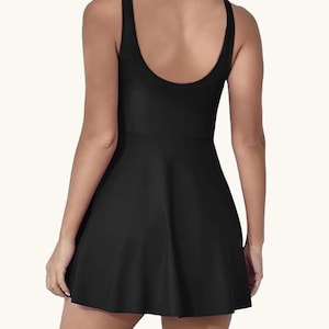 May include: Black one-piece swimsuit with a scoop back and a flared skirt. The sleeveless design and the skirt give the swimsuit a dress-like appearance. The swimsuit is made of a smooth, solid black fabric.