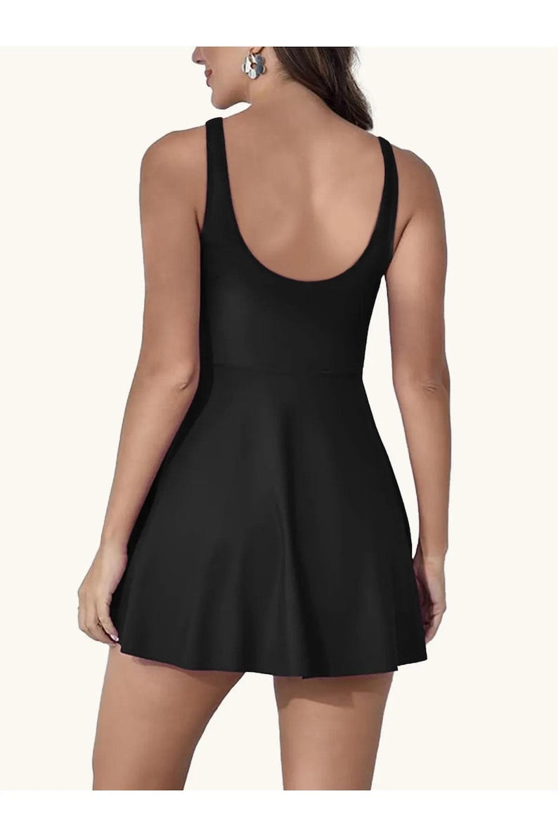 May include: Black one-piece swimsuit with a scoop back and a flared skirt. The sleeveless design and the skirt give the swimsuit a dress-like appearance. The swimsuit is made of a smooth, solid black fabric.