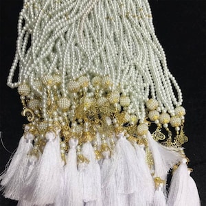 May include: A group of white pearl prayer beads with gold accents and white tassels. The beads are strung on a white cord and have a gold charm at the end.