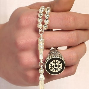 Peut inclure: Un chapelet de prière en argent avec un pompon et une bague en argent avec un motif noir et or.