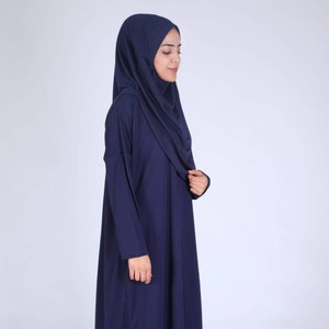 May include: A navy blue abaya and hijab set. The long-sleeved abaya has a loose fit, and the matching hijab drapes over the head and shoulders. The outfit is made of a soft, flowing fabric, suitable for modest wear.