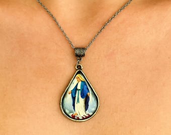 May include: Silver-toned necklace featuring a teardrop pendant with a religious image. The pendant depicts a figure in a blue robe and white dress. The chain is a delicate link style, and the pendant has an ornate bail.