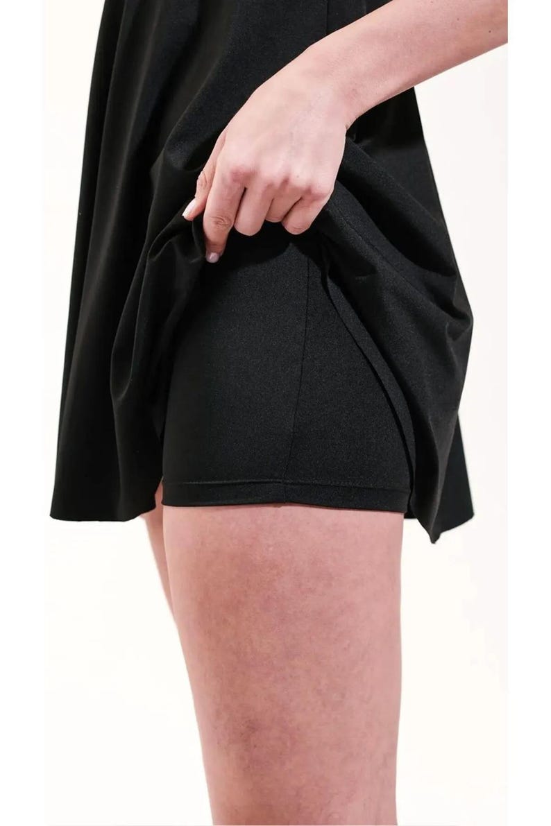 May include: A black athletic skort, featuring a flared skirt over built-in shorts. The fabric appears to be a smooth, matte material. The image shows a close-up of the garment, highlighting the design and construction.