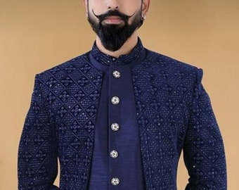 Puede incluir: Un hombre lleva una kurta azul marino con estampado y una chaqueta a juego. La kurta tiene un cuello mandarín y botones plateados. El hombre lleva pantalones blancos y zapatos blancos.
