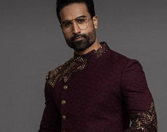 May include: A maroon long-sleeved kurta with gold embellishments on the shoulders and sleeves. The kurta has a high collar and a button closure. The model is wearing black trousers and black embellished loafers.