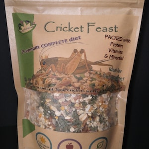 May include: A brown paper bag with a clear window showing a cricket food mix. The bag has a green and white logo with the text "Keptanicals" and the text "Cricket Feast Premium COMPLETE diet". The bag also has the text "PACKED with Protein, Vitamins & Minerals! Ideal for Gut-loading! The Gold Standard: Your crickets will feast like royalty!" and "Gut-Load NET WT. 12oz (340.2g) All Natural".