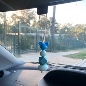 May include: A blue and white silicone car charm with a Mickey Mouse head and geometric beads hanging from a white string.